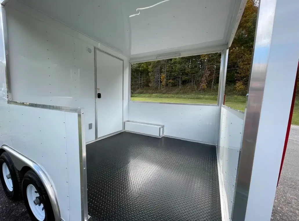 Interior of an empty trailer with a black textured floor and large open side window.