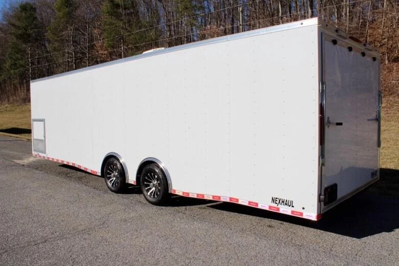 White Nexhaul enclosed trailer with dual axles and a rear door, parked on a paved road.